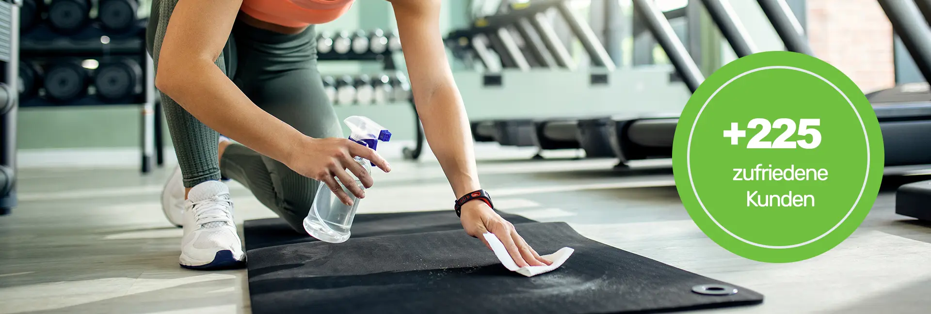 Fitnesstudioreinigung -Frau mit orangenem Kurzoberteil mit Sprühflasche, desinfiziert eine Gummimatte - Clean Team